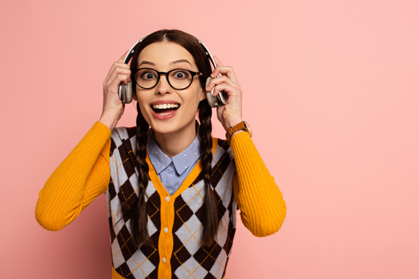 excited female nerd in eyeglasses listening music with headphones on pink - Fotó, kép