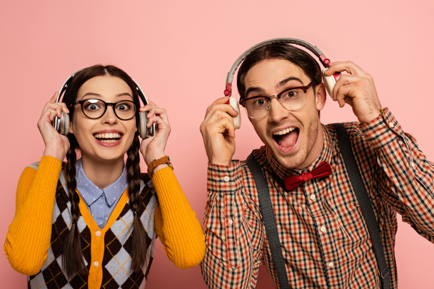 couple of excited nerds in eyeglasses listening music with headphones on pink - Foto, Imagen