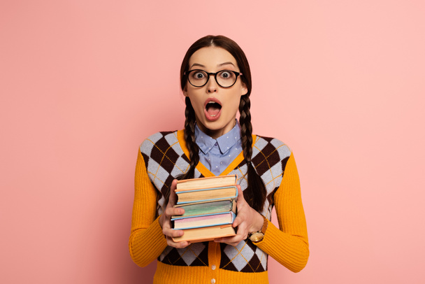 šokovaný ženský nerd s otevřenými ústy drží knihy na růžové - Fotografie, Obrázek