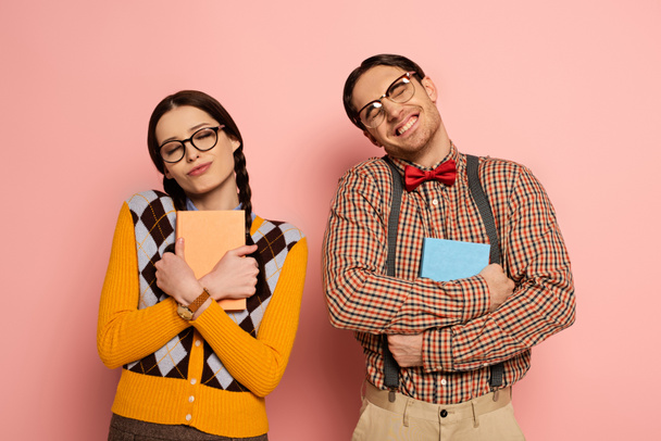 couple of cheerful nerds in eyeglasses hugging books on pink - Photo, Image
