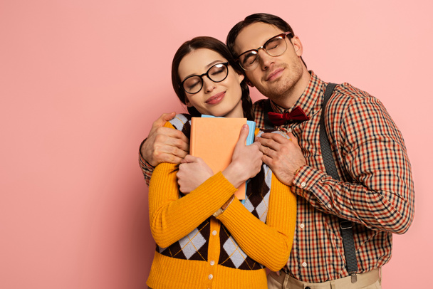 šťastný nerd se zavřenýma očima objímání přítelkyně s knihami na růžové - Fotografie, Obrázek