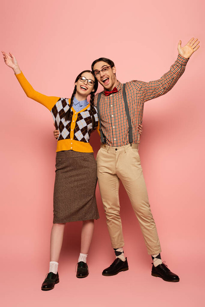 couple of cheerful nerds in eyeglasses gesturing and hugging on pink - Photo, image