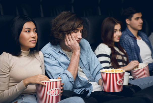 Yakışıklı genç adam sinemada film izlerken sıkılıyor. - Fotoğraf, Görsel