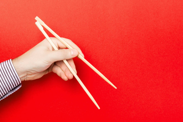 Wooden chopsticks holded with male hands on red background. Ready for eating concepts with empty space. - Foto, Imagem