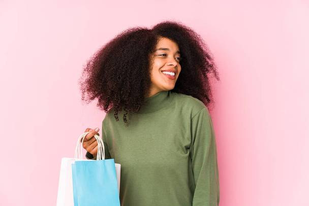 Junge Afro-Frau einkaufen isoliert Junge Afro-Frau einkaufen Isolationjunge Afro-Frau hält eine Rose isoliert blickt lächelnd, fröhlich und angenehm zur Seite. - Foto, Bild