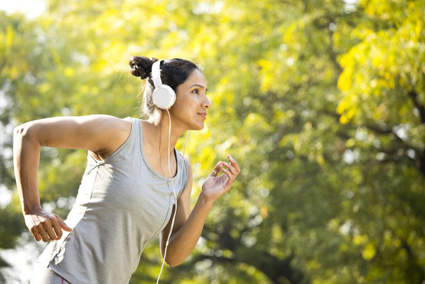 Sportswoman listening music and jogging at park - Φωτογραφία, εικόνα