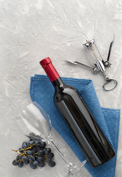 Wine bottle, wine glass, bunch of blue grapes and corkscrew on gray textured background. Flat lay. Top view. Copy space. - Photo, Image