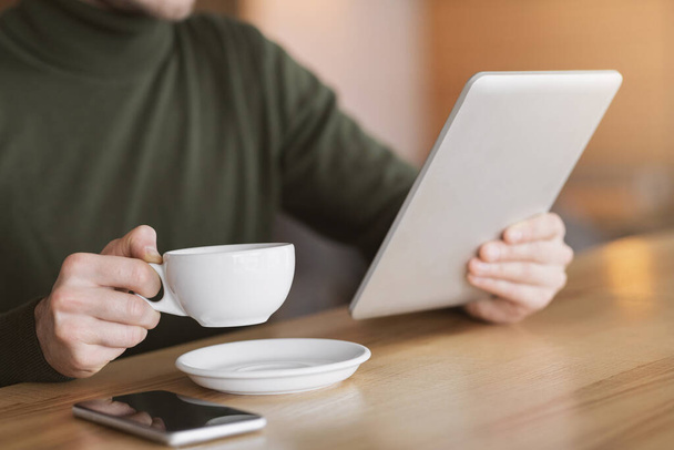 Male hands holding cup of tea and digital tablet - Foto, Imagen