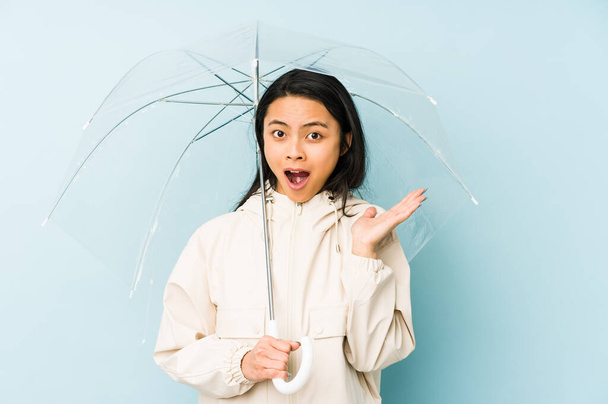 Young chinese woman holding an umbrella isolated screaming very angry and aggressive. - Φωτογραφία, εικόνα
