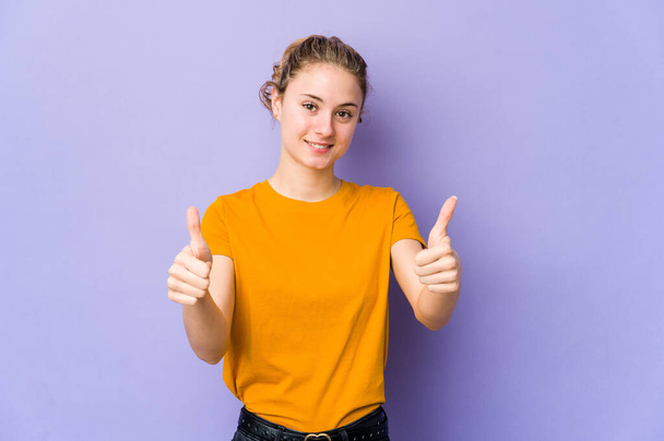 Young caucasian woman on purple background smiling and raising thumb up - Фото, зображення