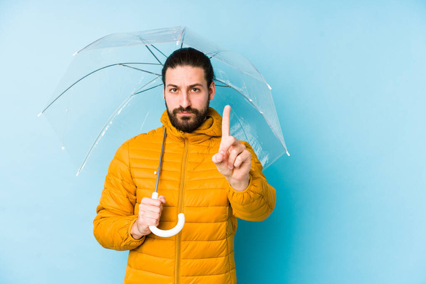 Молодий чоловік у довгому волоссі виглядає, тримаючи парасольку ізольовано, показуючи номер один пальцем
. - Фото, зображення