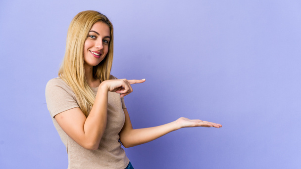 Young blonde woman isolated on purple background excited holding a copy space on palm. - Photo, Image