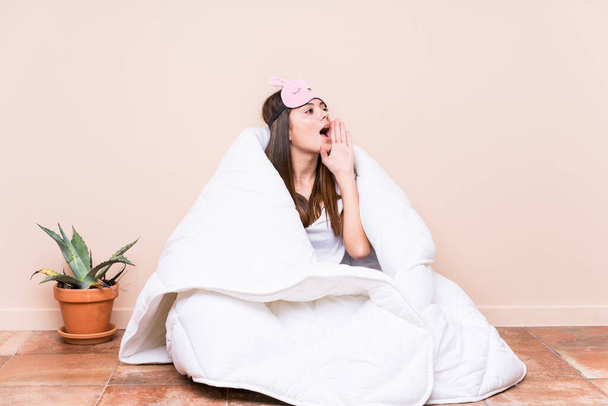 Молодая белая женщина отдыхает с одеялом крича и держа ладонь у открытого рта
. - Фото, изображение