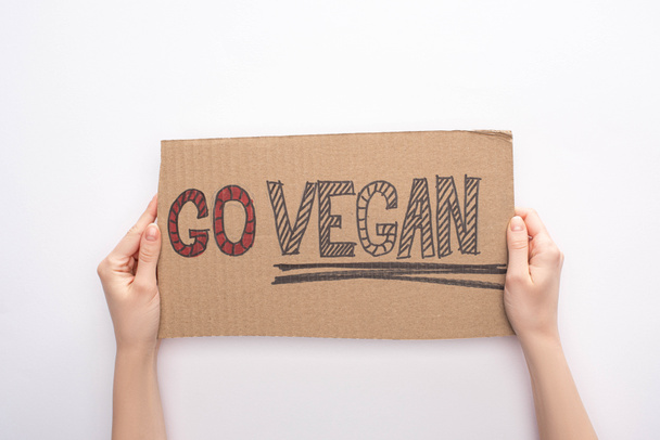 partial view of woman holding cardboard sign with go vegan inscription on white background - 写真・画像