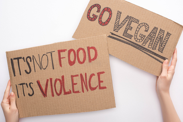 partial view of woman holding cardboard signs with go vegan and its not food its violence inscriptions on white background - Photo, Image