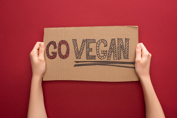 partial view of woman holding cardboard sign with go vegan inscription on red background - Φωτογραφία, εικόνα