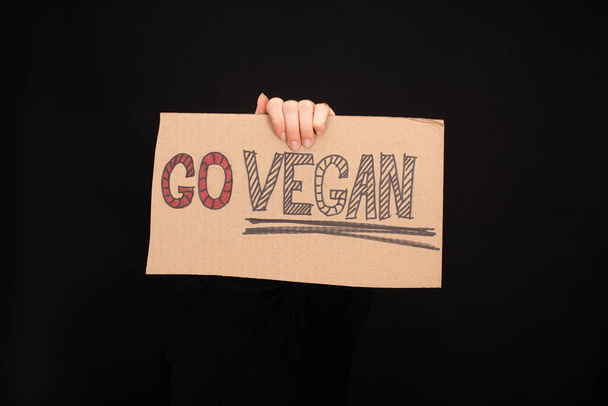 částečný pohled na ženu držící kartónový nápis s go veganským nápisem izolovaným na černé - Fotografie, Obrázek