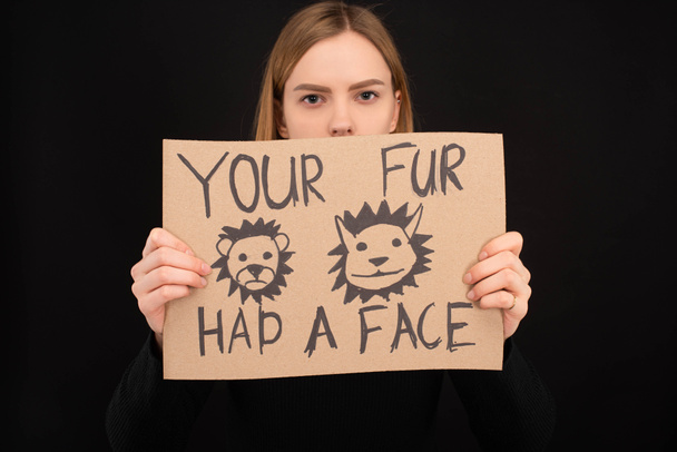 woman with obscure face holding cardboard sign with your fur had a face inscription isolated on black - Photo, Image