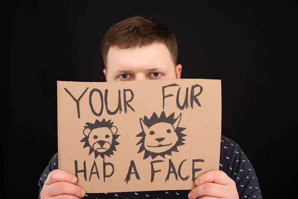 man with obscure face holding cardboard sign with your fur had a face inscription isolated on black - Photo, Image