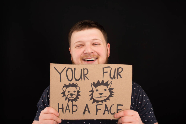 happy smiling man holding cardboard sign with your fur had a face inscription isolated on black - Photo, Image
