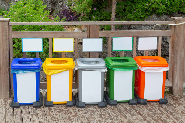 Концепция сегрегации отходов. Разноцветные мусорные баки для сбора отдельного мусора на фоне природы. Цветные контейнеры для сбора мусора в парке
. - Фото, изображение