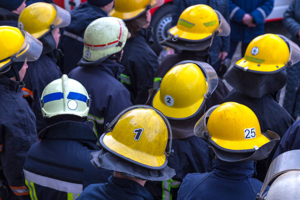 Bomberos en barricas con números personales. Primer plano de la multitud de bomberos en cascos protectores amarillos
. - Foto, Imagen