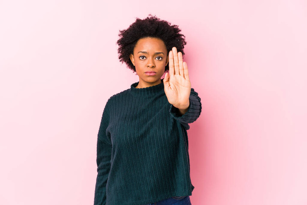 Mujer afroamericana de mediana edad sobre un fondo rosa aislado de pie con la mano extendida que muestra señal de stop, lo que le impide
. - Foto, Imagen