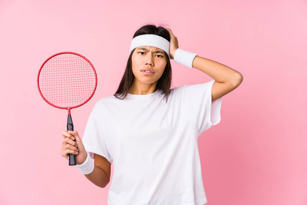 Junge Chinesin spielt Badminton vor rosa Hintergrund ist schockiert und erinnert sich an wichtiges Treffen. - Foto, Bild