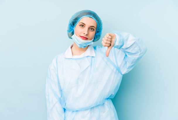 Νεαρή χειρούργος γυναίκα απομονωμένη δείχνει μια χειρονομία αντιπάθειας, χωρίς αντίχειρες. Έννοια διαφωνίας. - Φωτογραφία, εικόνα