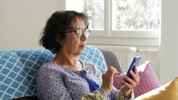 vrolijk brunette senior vrouw met behulp van smartphone terwijl zitten op de bank - Video