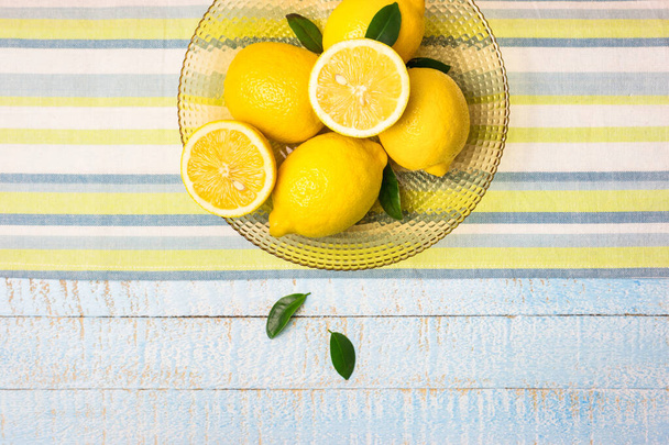 Schüssel mit frischen ganzen und halben Zitronen auf hellblauem Holzgrund. Draufsicht mit Kopierraum. - Foto, Bild