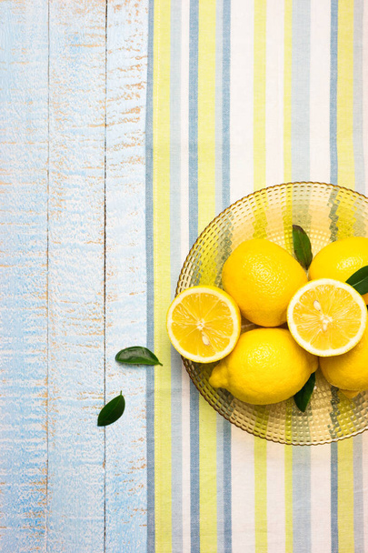 Bowl with fresh whole and half lemons on light blue wooden background. Top view with copy space. - Fotoğraf, Görsel