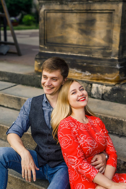 una joven pareja está elegantemente vestida, una chica con un vestido rojo, un hombre con una camisa azul y pantalones azules, sentarse en las escaleras
 - Foto, imagen