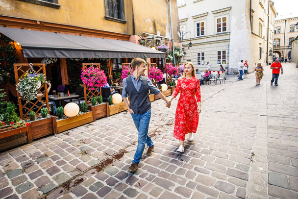a young couple is stylishly dressed, a girl in a red dress, a man in a blue shirt and blue pants, walk the streets in Krakow Poland - Foto, afbeelding