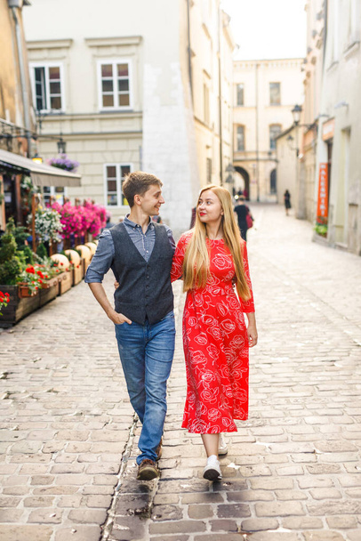 a young couple is stylishly dressed, a girl in a red dress, a man in a blue shirt and blue pants, walk the streets in Krakow Poland - Photo, image