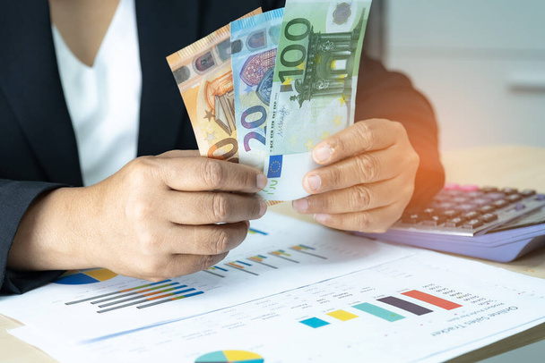 Asian accountant holding Euro banknotes, working, calculate and analyzing report project accounting with calculator and graph report in modern office : finance and business concept. - Foto, Imagem
