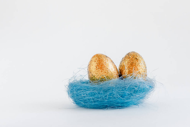 Huevos dorados de Pascua en el nido sobre fondo blanco. Mínimo espacio de copia de concepto de Pascua para texto. Vista superior, plano
. - Foto, Imagen
