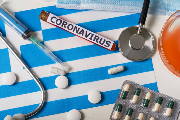 Coronavirus, ncov koncept. Horní pohled ochranné dýchací masky, stetoskop, injekční stříkačka, pilulky na vlajce Řecka. Nový výskyt čínského koronaviru - Fotografie, Obrázek