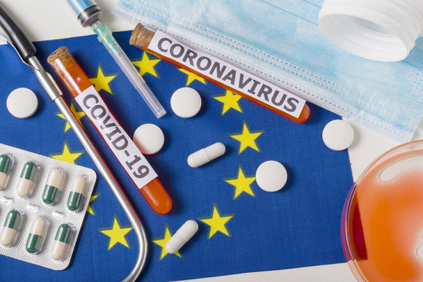 Coronavirus, el concepto COVid-19. Vista superior máscara respiratoria protectora, estetoscopio, jeringa, pastillas en la bandera de Europa. Un nuevo brote del coronavirus chino
 - Foto, Imagen