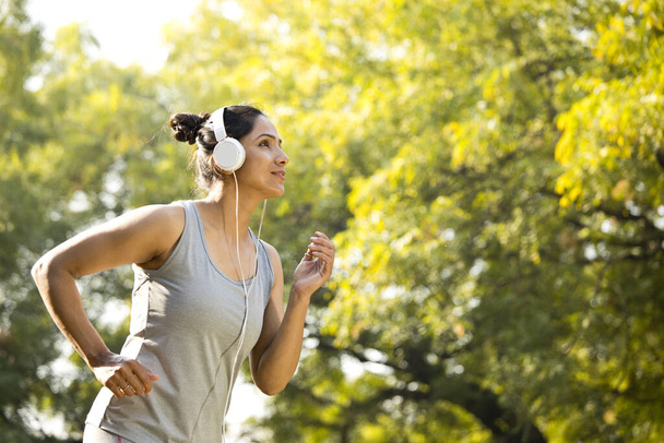 Sportswoman listening music and jogging at park - Φωτογραφία, εικόνα