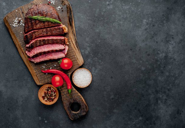 grilled beef steak with spices, tomatoes and herbs on dark background - Фото, изображение