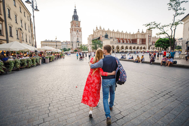 um jovem casal está elegantemente vestido, uma menina em um vestido vermelho, um homem com uma camisa azul e calças azuis, andar pelas ruas em Cracóvia Polônia
 - Foto, Imagem