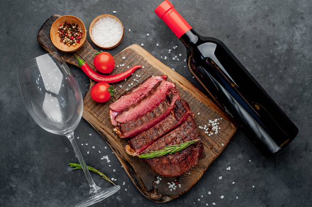 wineglass, bottle of wine, grilled beef steak with spices, tomatoes and herbs on dark background - Foto, immagini