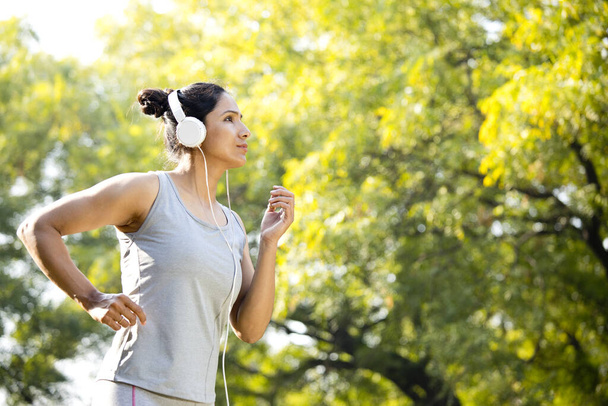 Sportswoman listening music and jogging at park - 写真・画像