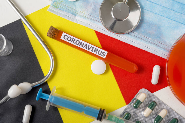 Coronavirus, nCoV concept. Top view protective breathing mask, stethoscope, syringe, pills on the flag of Belgium. A new outbreak of the Chinese coronavirus - Photo, Image