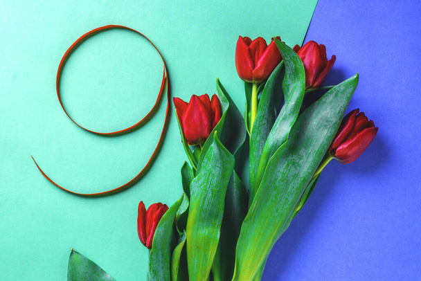 kreativní tónovaný červený hedvábný stuha ve tvaru čísla devět, s tulipány květiny, slavnostní pohlednice na modrém pozadí - Fotografie, Obrázek