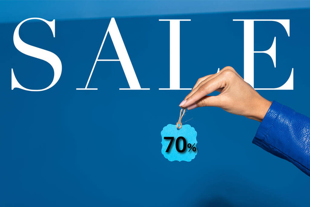 cropped view of african american woman holding label on blue background, 70 percent sale illustration - 写真・画像
