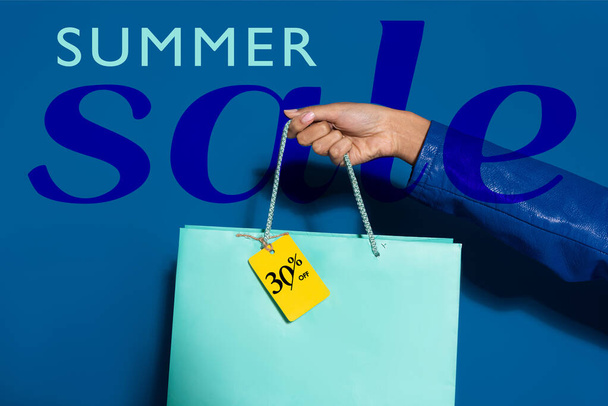 vista ritagliata della donna afro-americana con borsa della spesa con etichetta su blu, illustrazione vendita estiva
  - Foto, immagini
