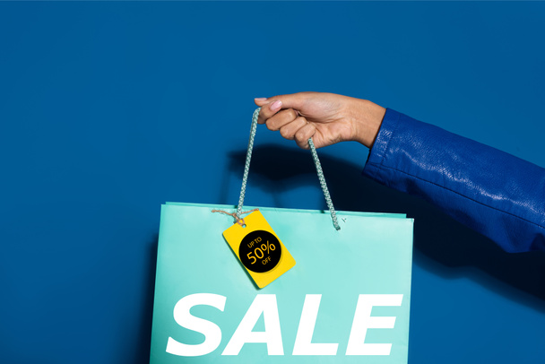 vista cortada da mulher americana africana segurando saco de compras com etiqueta em azul, 50 por cento ilustração venda
 - Foto, Imagem