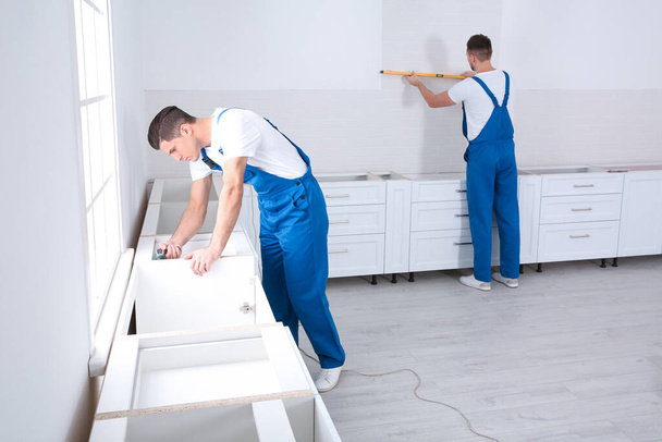 Maintenance workers installing new kitchen furniture indoors - Фото, изображение